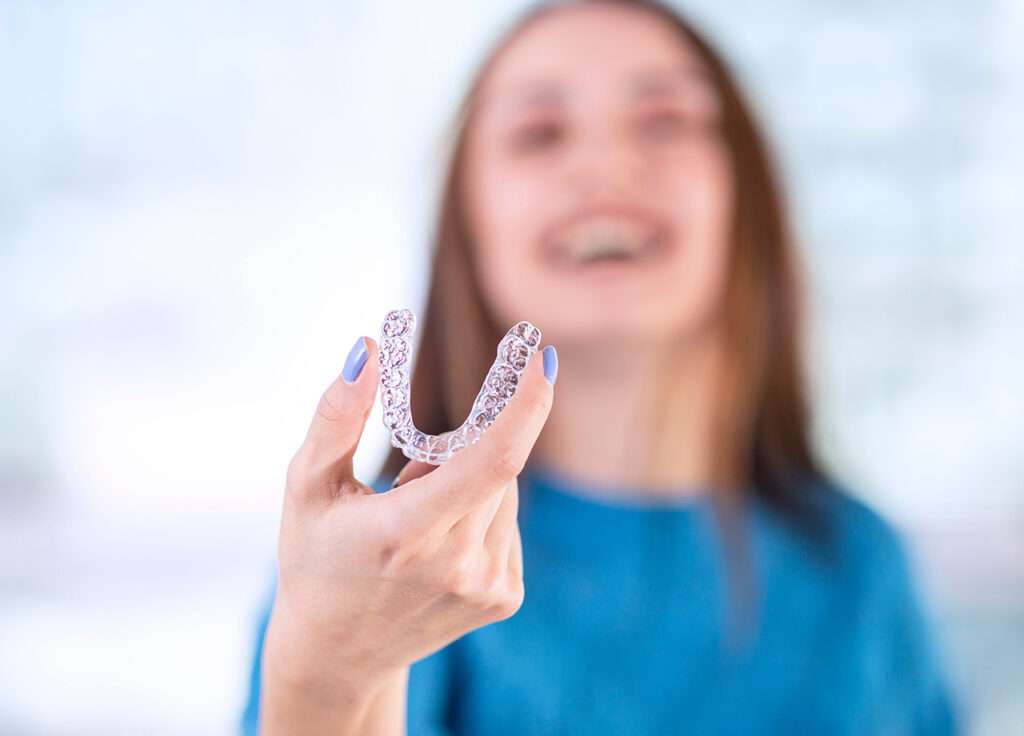 Woman smiling while holding a clear aligner in her hand.