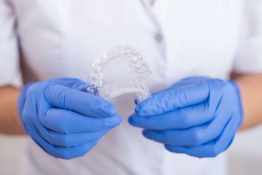 A doctor wearing gloves and holding a pair of clear aligners.