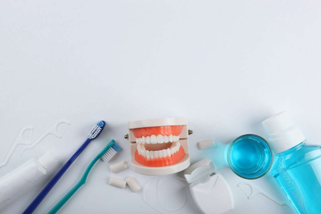 A teeth model next to floss, toothpaste, toothbrushes, and mouthwash.