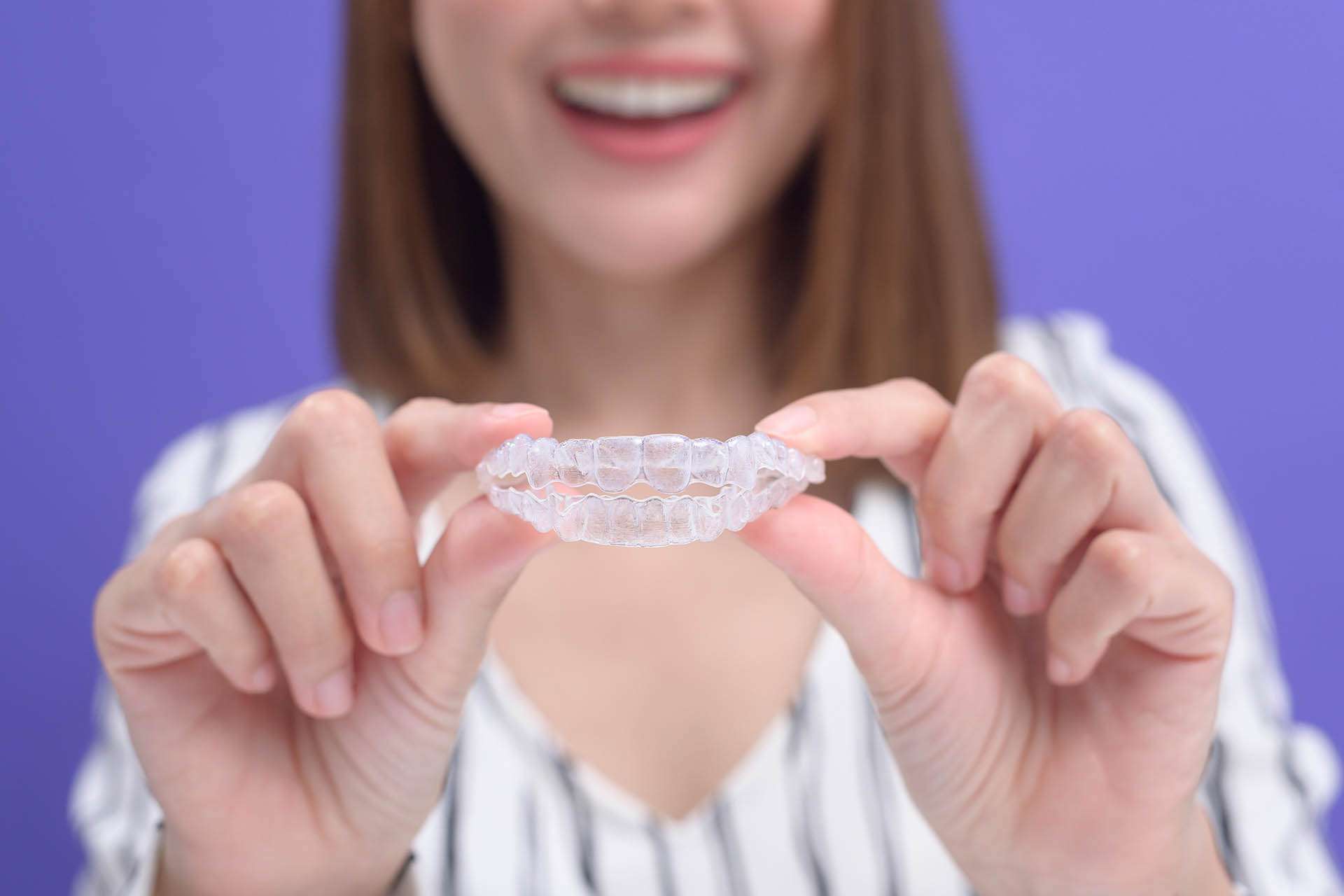 Woman smiling and holding up her clear aligners.