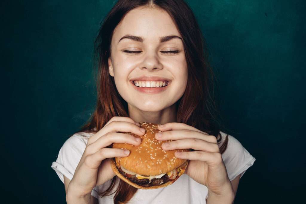 Woman smiling and holding a hamburger in her hands.