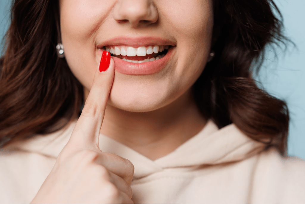 A smiling woman points to her straight, white teeth. Only the bottom half of her face is visible