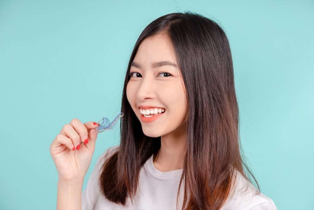 A smiling woman holds up a blue retainer.