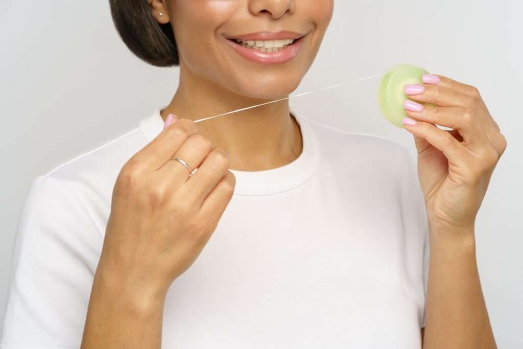 A woman in a white t-shirt flosses her teeth.