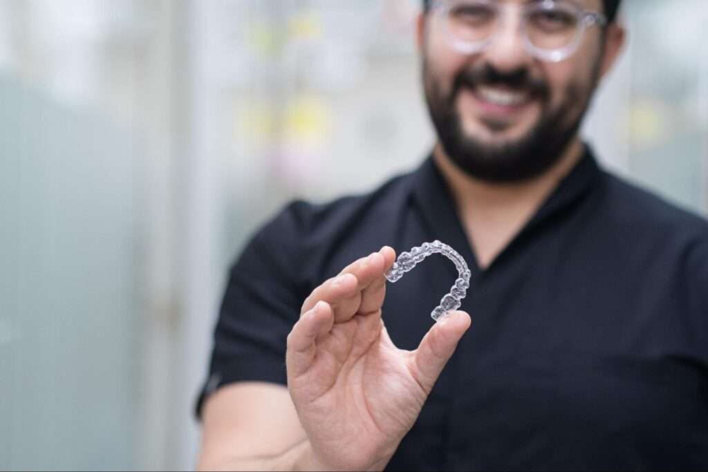 A dentist holds up a clear aligner and smiles.