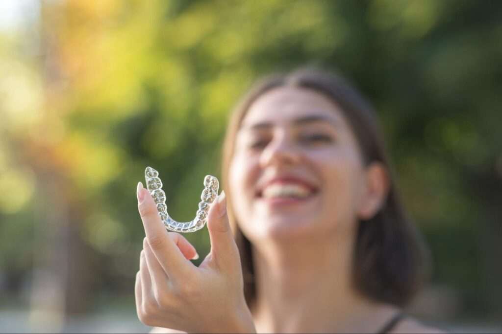 Woman holding a retainer with trees in the background. 