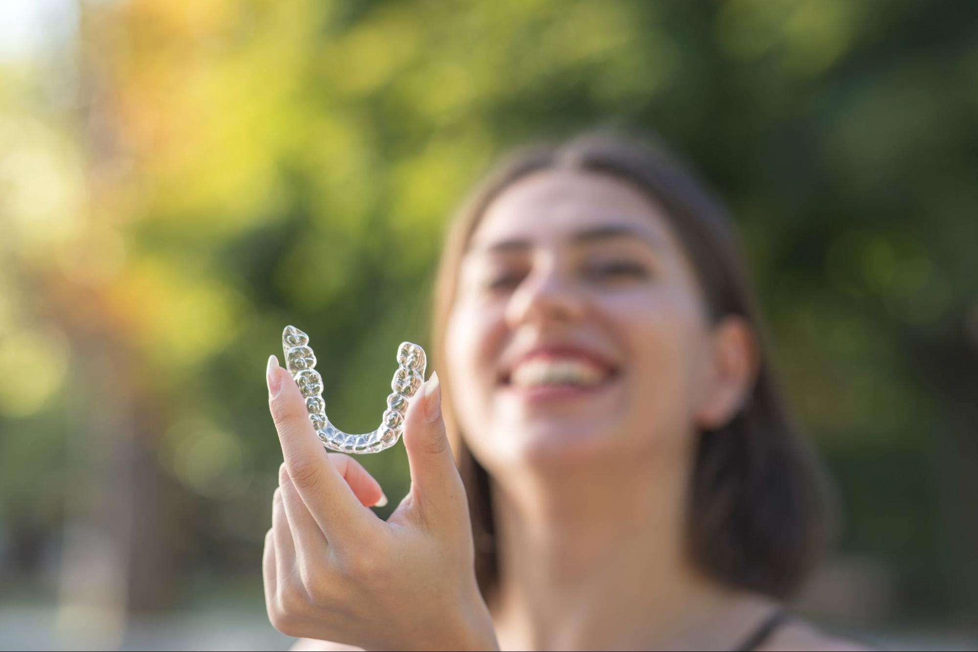 smiling woman holding clear aligner