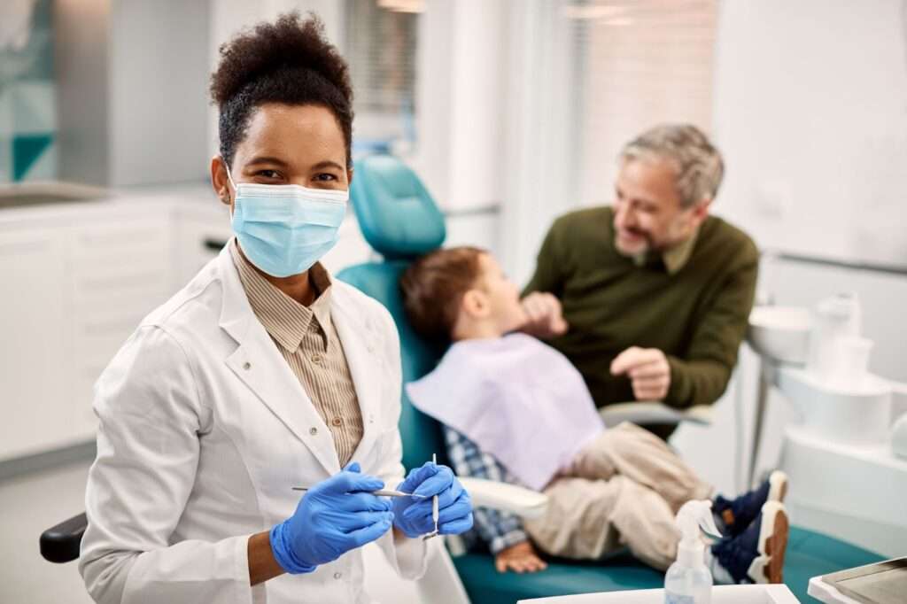 A woman in a dental mask and gloves holding a child's hand.