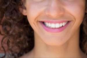 A close-up shot of a girl with curly brown hair, smiling and showing her healthy white teeth.