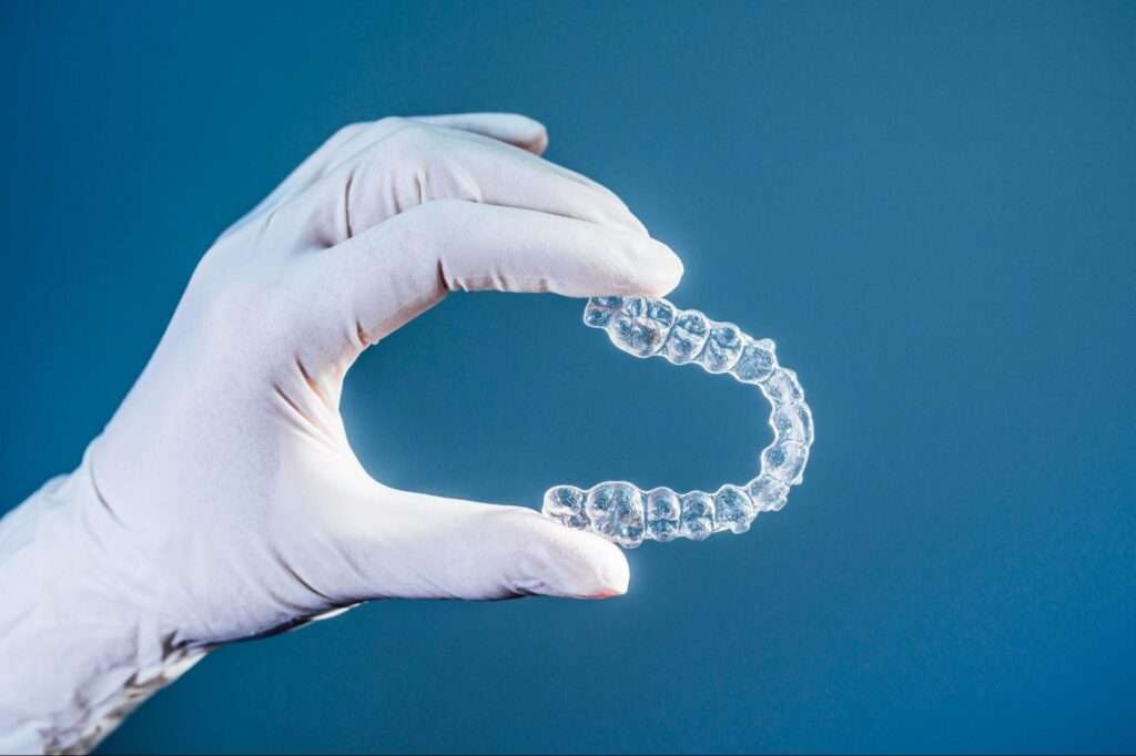 Gloved hand holding clear aligners.