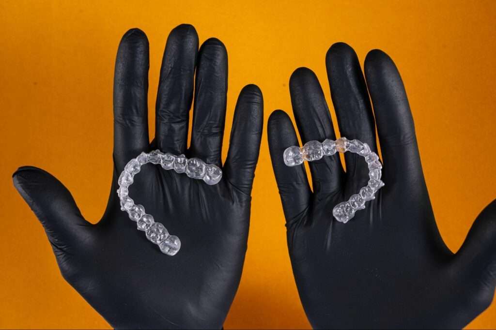 A closeup shot of hands wearing black gloves holding a pair of clear dental retainers.