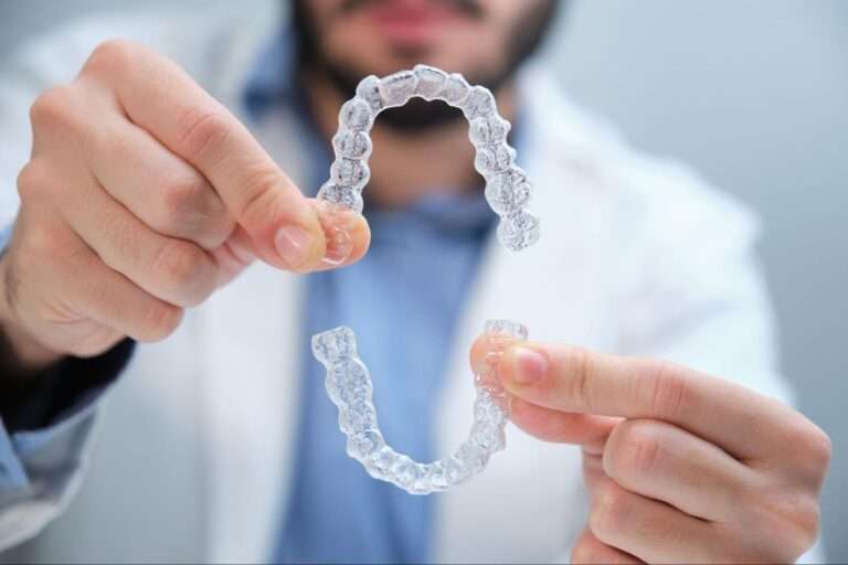 A male orthodontist holding a pair of clear retainers.